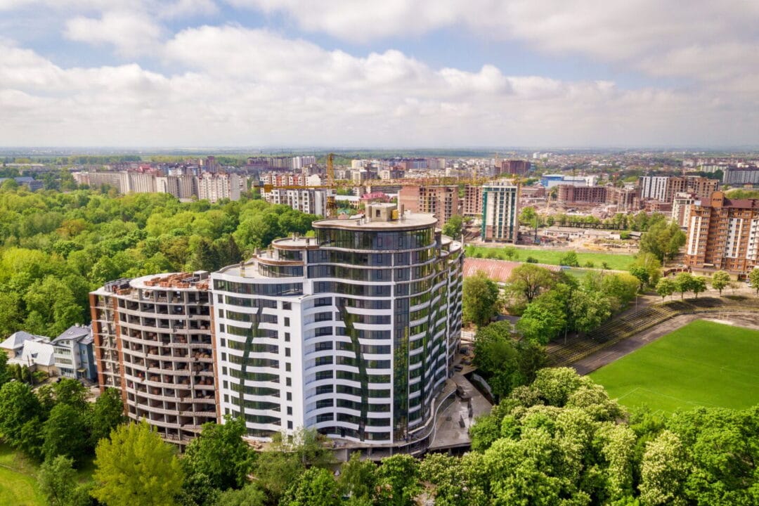 apartment or office tall building unfinished under construction among green tree tops e1737480941739